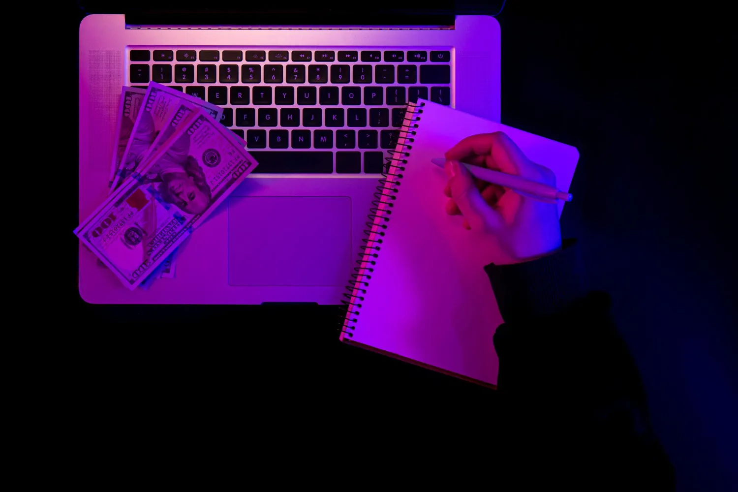 laptop-blank-notepad-and-paper-money-in-neon-lighting-top-view